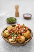 A delicious bowl of roasted new potatoes is garnished with bacon, fresh herbs, chopped onions, and