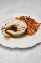 A generous portion of tender white fish is plated alongside a colorful mix of sautéed tomatoes and