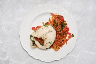 A succulent piece of cod fish garnished with vegetables rests on a beautiful white plate