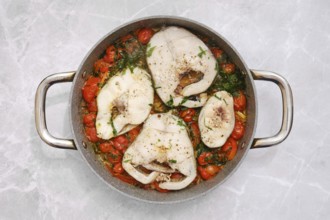 Cod fish fillets are gently simmering in a tangy tomato sauce, accompanied by vibrant cherry