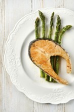 Grilled salmon on a round white dish alongside roasted asparagus spears. The vibrant green