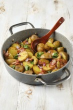 Golden-brown potatoes mixed with crispy bacon, fresh herbs, and onions are presented in a stovetop