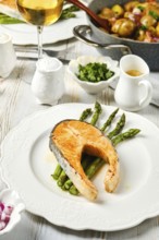A perfectly cooked salmon steak rests on a bed of crispy asparagus. Accompanied by fresh herbs and