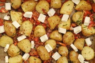 Colorful roasted potatoes and red peppers are arranged on a baking tray, topped with cubes of feta