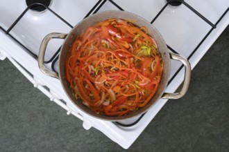Freshly sliced bell peppers, carrot and onions simmer in a pot on the stove in a cozy kitchen