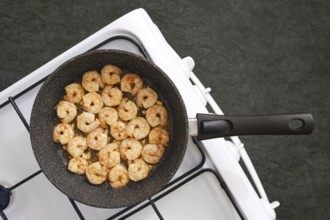 A frying pan on a stovetop filled with perfectly cooked shrimp in a kitchen. The shrimp are