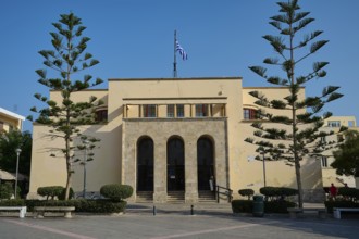 Archaeological Museum, Symmetrical beige building with Greek flag and tall trees, under clear sky