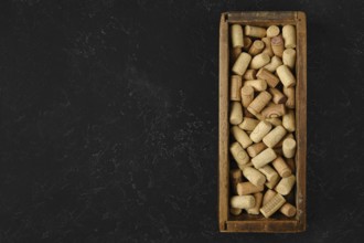 A wooden box filled with assorted wine corks rests on a dark surface. The corks vary in size and