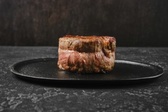 A perfectly cooked filet mignon rests on a sleek black plate, showcasing its rich color and