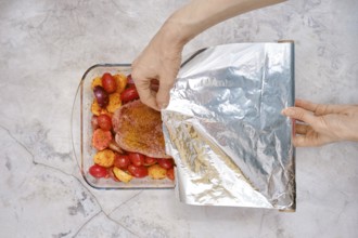 A hand gently covers a baking dish filled with seasoned turkey breast and juicy vegetables with