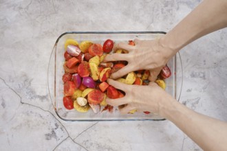 Hands mix together seasoned potatoes, tomatoes, and onions in a glass dish for a turkey breast