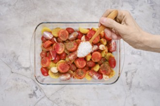 A hand sprinkles salt over colorful fresh vegetables and seasonings, preparing a vibrant mix to