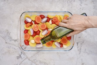 Pouring olive oil on slices of fresh vegetables including tomatoes, carrots, potatoes and onions