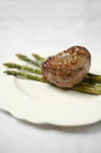 Filet mignon is grilled to perfection and presented on a white plate atop freshly cooked asparagus.