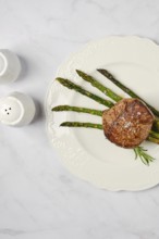 A perfectly cooked filet mignon sits elegantly on a white plate alongside vibrant asparagus spears.