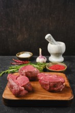 Several cuts of fresh beef tenderloin are arranged on a wooden cutting board, surrounded by spices