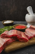 A selection of raw beef ribs is arranged on a wooden cutting board alongside bowls of seasoning.