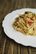 A plate of seafood spaghetti features fresh pasta topped with shrimp, mussels, and vegetables. It