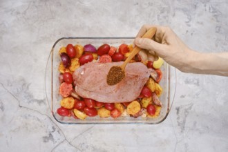 A hand sprinkles a blend of spices over a raw turkey breast resting on a bed of vibrant red and