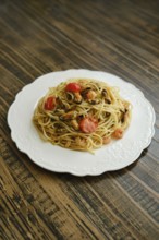 A serving of spaghetti topped with fresh seafood and cherry tomatoes is showcased on a white plate
