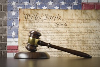 United states constitution and american flag on wall with gavel resting on table in front