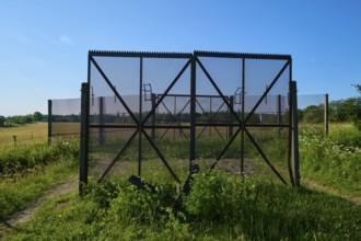 Border fence of the former inner-German border, surrounded by green meadows under a clear blue sky,