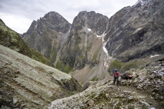 Mountaineer on steep rocky mountain landscape with fresh snow in summer, behind mountain peaks