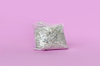 Small plastic bag containing ash of a pet cat after cremation on pink background
