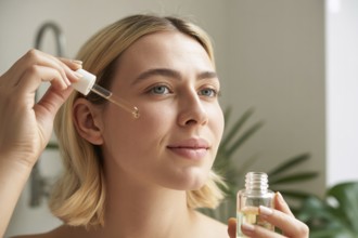 Close up of blond woman applying face serum with glass dropper. Highlights glowing skin and natural