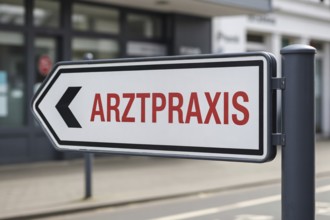 Close up of modern clean direction sign with red text Arztpraxis in sunny outdoor setting.