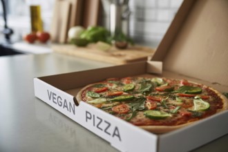 Freshly delivered vegetable pizza in box labeled vegan pizza on kitchen counter. Healthy