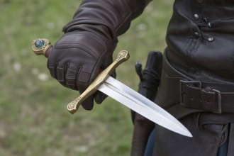 Hand in leather glove holding medieval dagger with gemstone. Concept of authentic medieval or LARP