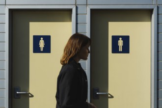 Transgender woman in front of men's and women's bathroom doors. Concept of public restroom access