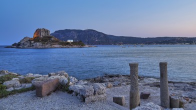 Ruins in the foreground and a calm sea with a rocky island at dusk, Agios Stefanos Beach, Agios