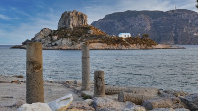 Ancient columns overlooking a rocky island with a blue house in the sea, Agios Stefanos Beach,