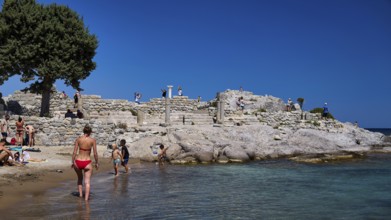 People exploring ancient ruins on the beach under a clear blue sky, Agios Stefanos Beach, Agios