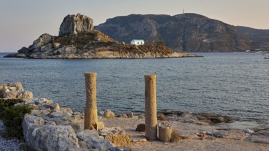 Ancient columns in front of the sea in warm evening light with an island in the background, Agios