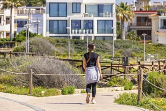 Young woman walking outdoors on a path in a residential area and listening to music with headphones