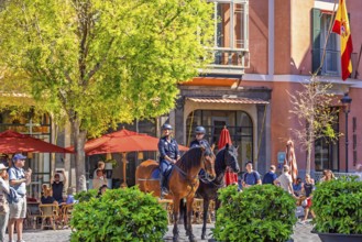 Mounted police officers sitting on horses in a town square with restaurants and people in the old