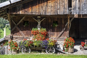 Colourful floral decorations and crucifix at a rustic alpine hut, Ridnauntal, South Tyrol, Italy