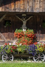 Colourful floral decorations and crucifix at a rustic alpine hut, Ridnauntal, South Tyrol, Italy