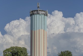 A tall water tower, painted with blue and white stripes, sits enthroned in a green landscape.