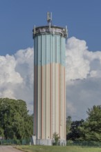 A tall water tower, painted with blue and white stripes, sits enthroned in a green landscape.