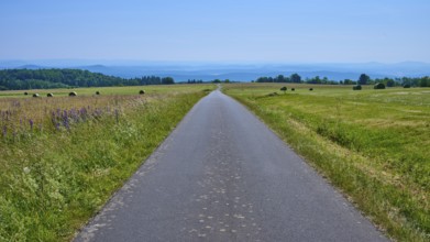 Endless road leads through green fields under a clear blue sky with hills in the distance,