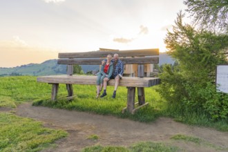 A couple sits on an oversized bench and enjoys the sunset, Alpe di Siusi, Dolomites, South Tyrol,