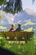 Couple sitting together on a bench and looking at the mountains, Alpe di Siusi, Dolomites, South