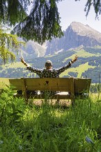 Person on a bench with outstretched arms in front of a mountain landscape, Alpe di Siusi,