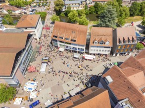 A lively, summery aerial view of a square with people, market stalls and surrounding buildings, 950
