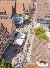 Aerial view of a busy street with half-timbered houses and cafés with parasols, many passers-by,