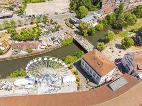 View from above of a summer festival with Ferris wheel, bridge and many people along a river in the